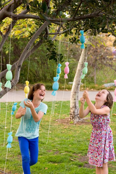 two little girls pulling down brightly colored paper eggs tied in a tree