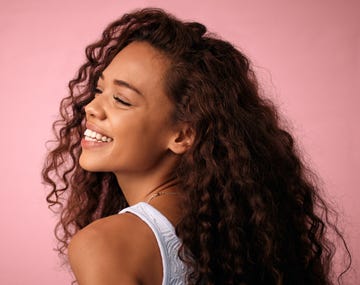 studio shot of a beautiful young woman with strong hair posing against a pink background
