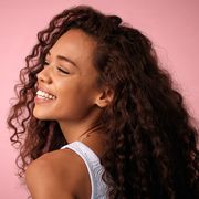 studio shot of a beautiful young woman with strong hair posing against a pink background