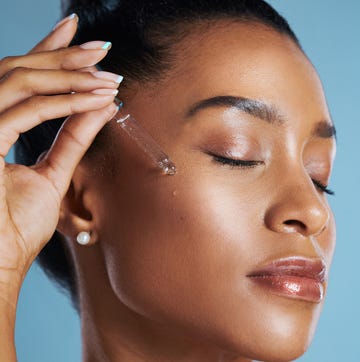 studio shot of a young woman applying an oil to her face against a blue background