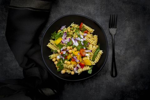 studio shot of bowl offusillipasta salad with chick peas, bell peppers, arugula, spanish onion, basil and parsley