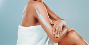 studio shot of woman wrapped in towel applying body lotion