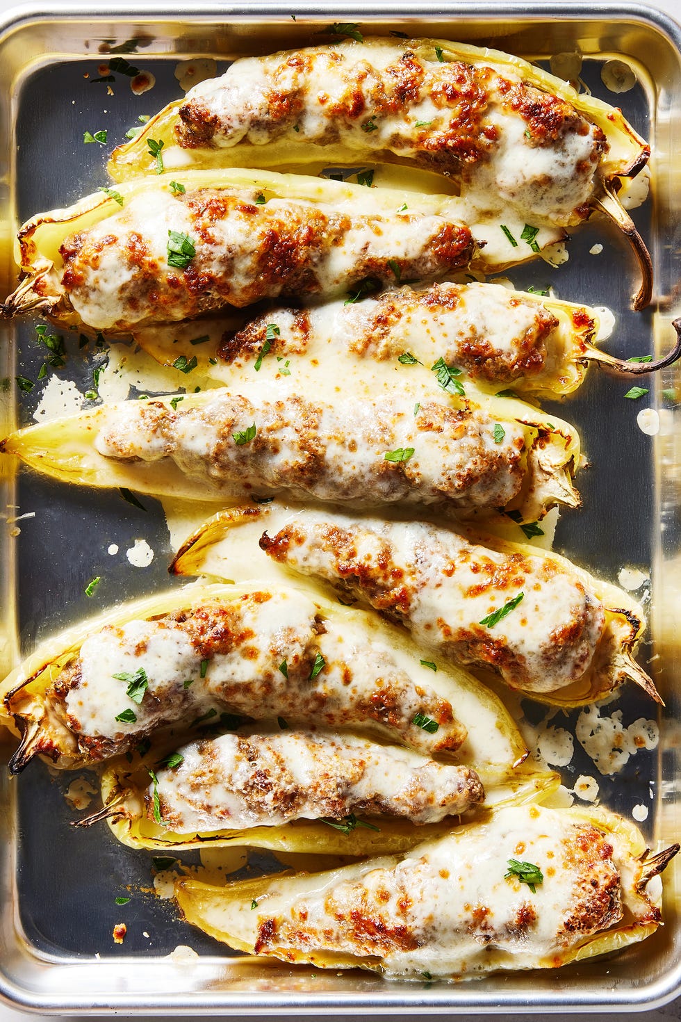Stuffed Banana Peppers banana peppers stuffed with pork and beef on a sheet pan topped with melted cheese