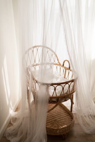 stylish scandinavian newborn baby nursery with natural rattan cradle and sheer white canopy hanging over it