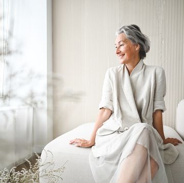 stylish senior woman enjoying a peaceful moment in her modern, minimalist apartment, looking out the window with a serene expression