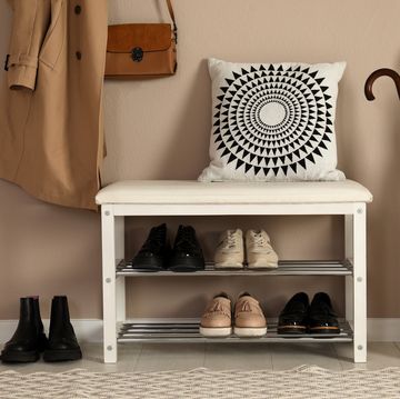 stylish storage bench with different pairs of shoes near beige wall in hall
