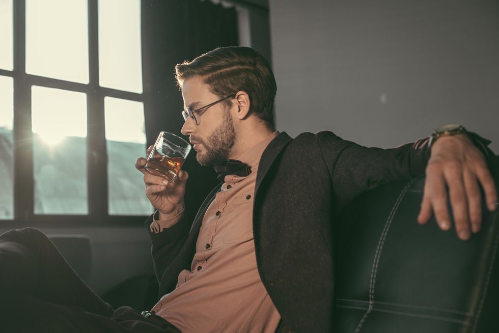 stylish young businessman in eyeglasses and bow tie drinking whiskey