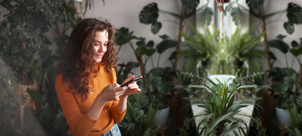stylish young woman with smartphone in room with plants copy space and banner