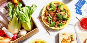 blue apron subscription services meal kit plated on marble table surrounded by vegetables in box and stirfry on yellow plates