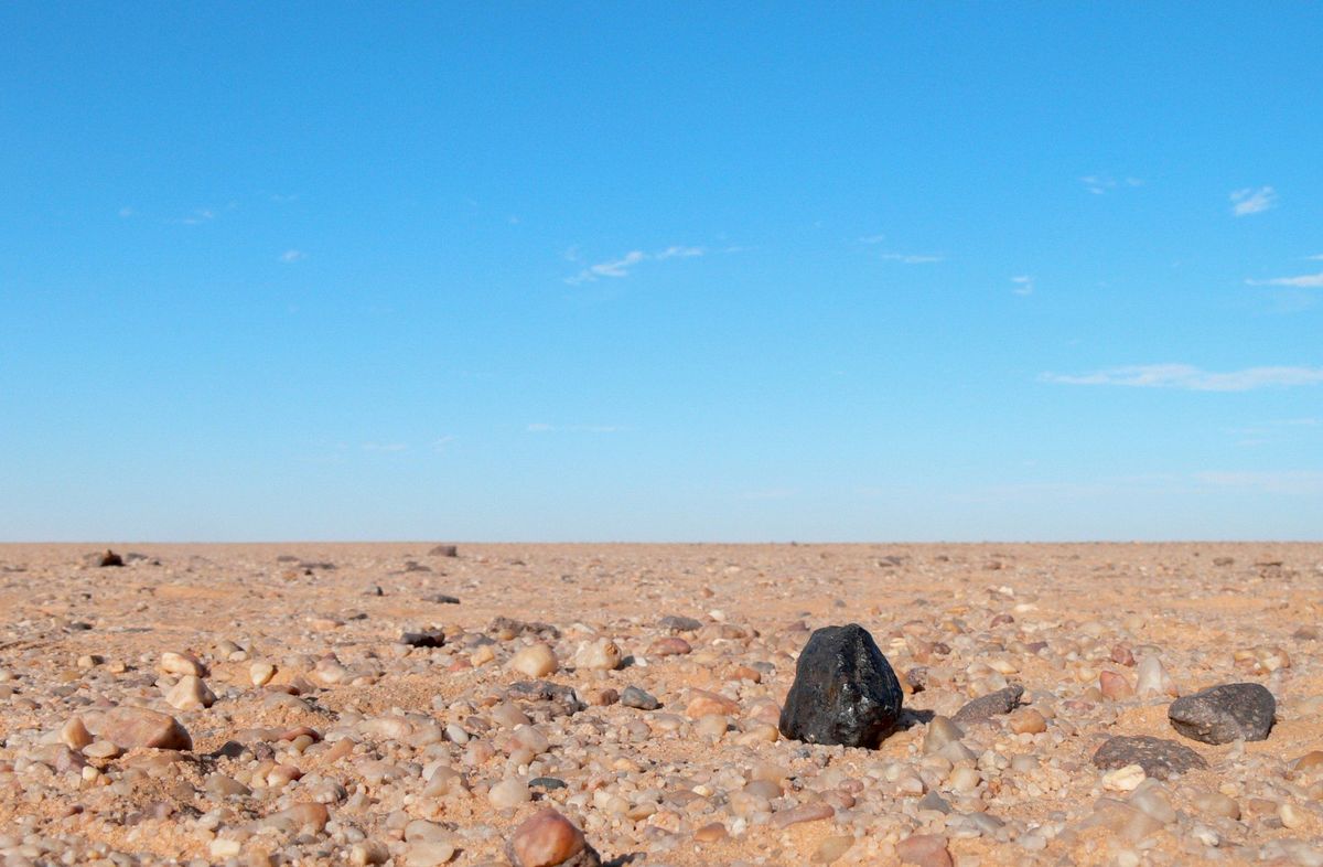 Een zwart stuk steen een meteorietsoort genaamd ureliet steekt scherp af tegen het lichtkleurige steengruis dat kenmerkend is voor de Nubische Woestijn in Soedan