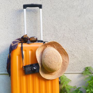 suit case ,straw hat camera in front of the wall