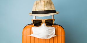 suitcase with hat, sunglasses and protective medical mask on pastel blue background minimal creative coronavirus covid 19 travel concept