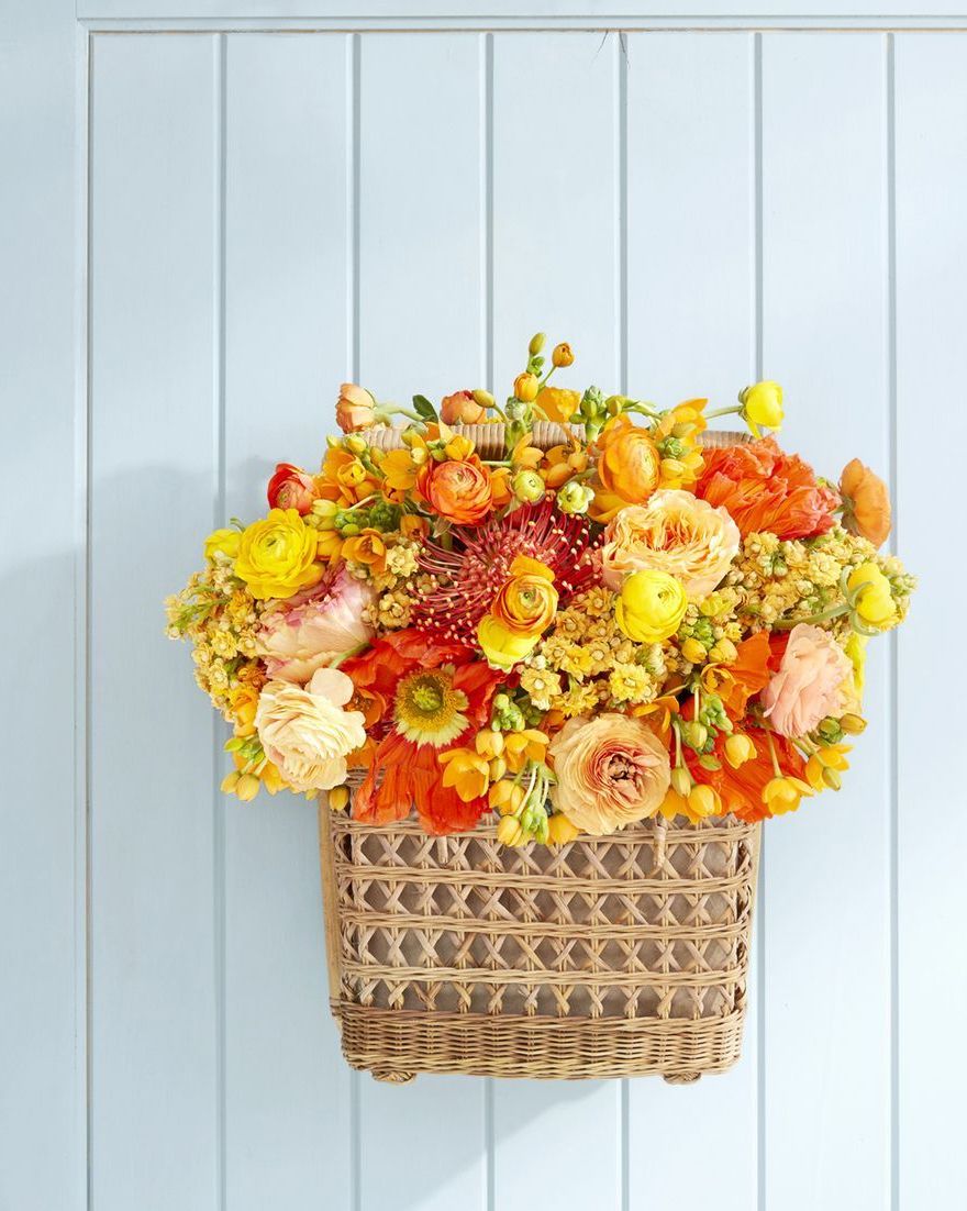 a rectangular basket hung on a light blue door filled with orange and yellow summer blooms