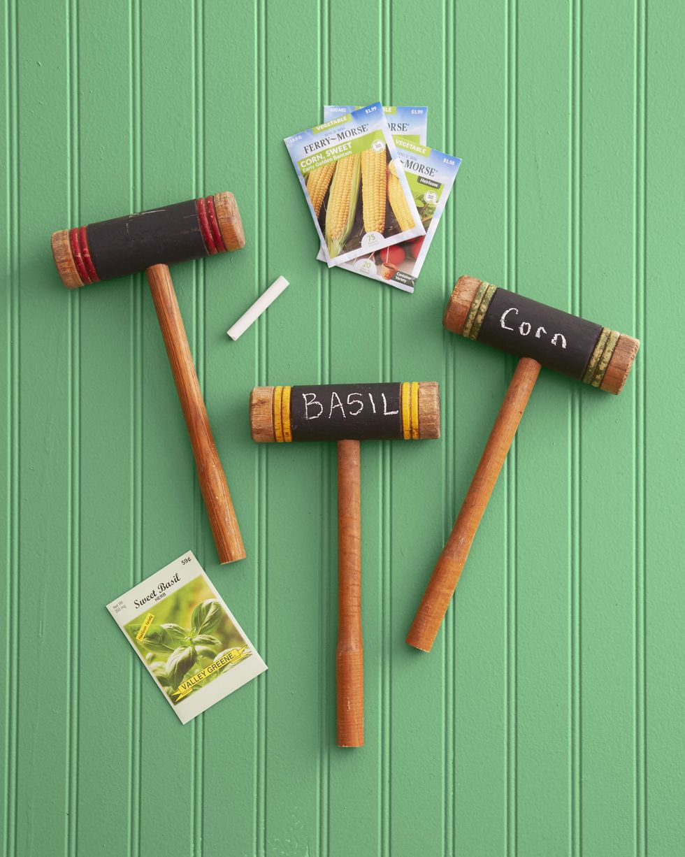 three croquet mallets turned into garden markers for a summer craft project with the words corn and basil written in chalk on the heads