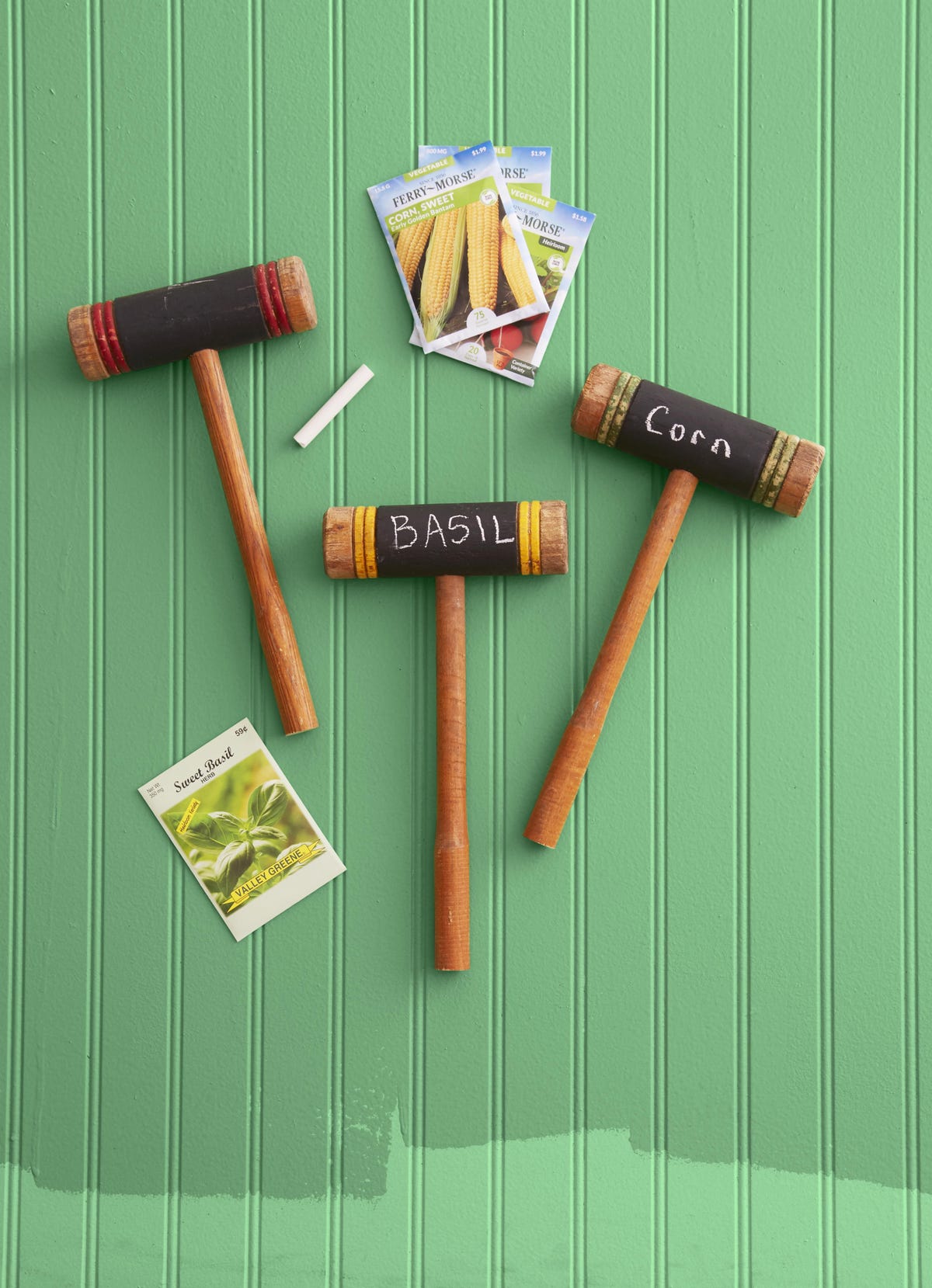 three croquet mallets turned into garden markers for a summer craft project with the words corn and basil written in chalk on the heads