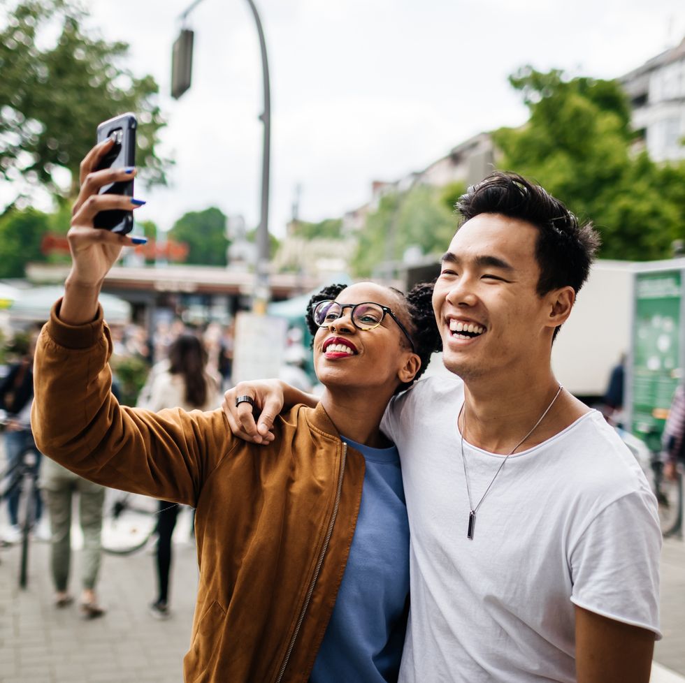 a young tourist couple standing in a new city take a photo of themselves using a smartphone