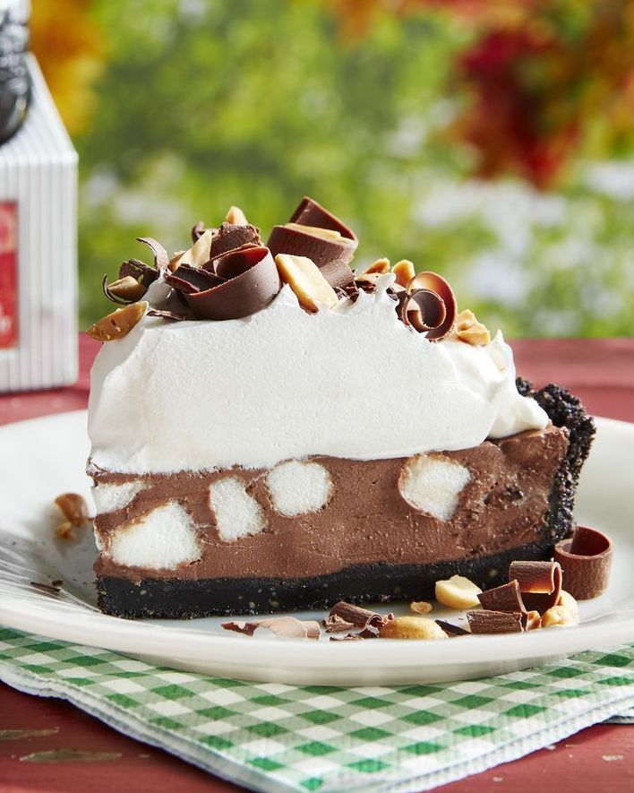 a slice of rocky road pie on a white plate and topped with whipped cream chopped peanuts and chocolate curls