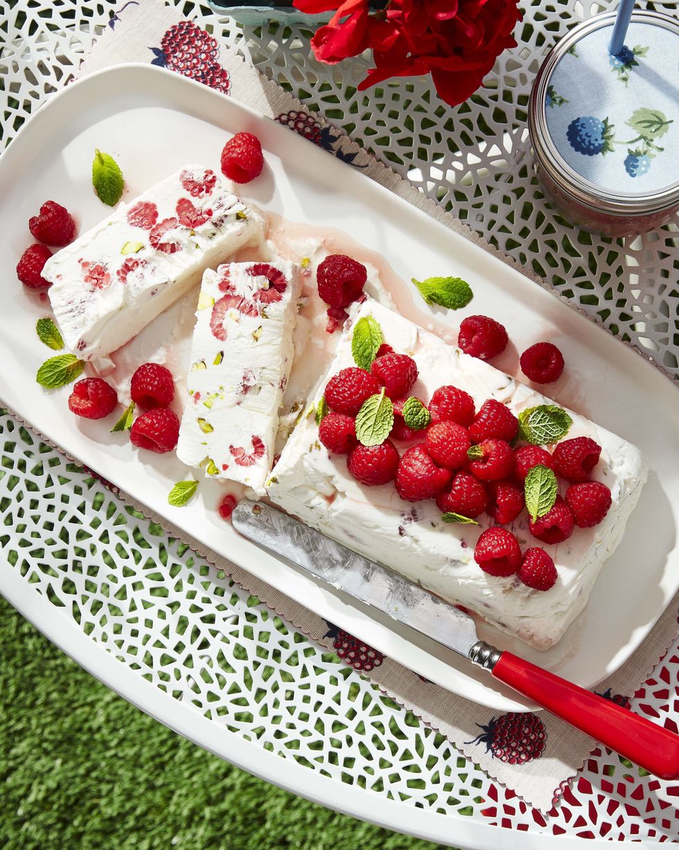 raspberry and pistachio semifreddo on a white serving plate and topped with fresh raspberries and mint leaves