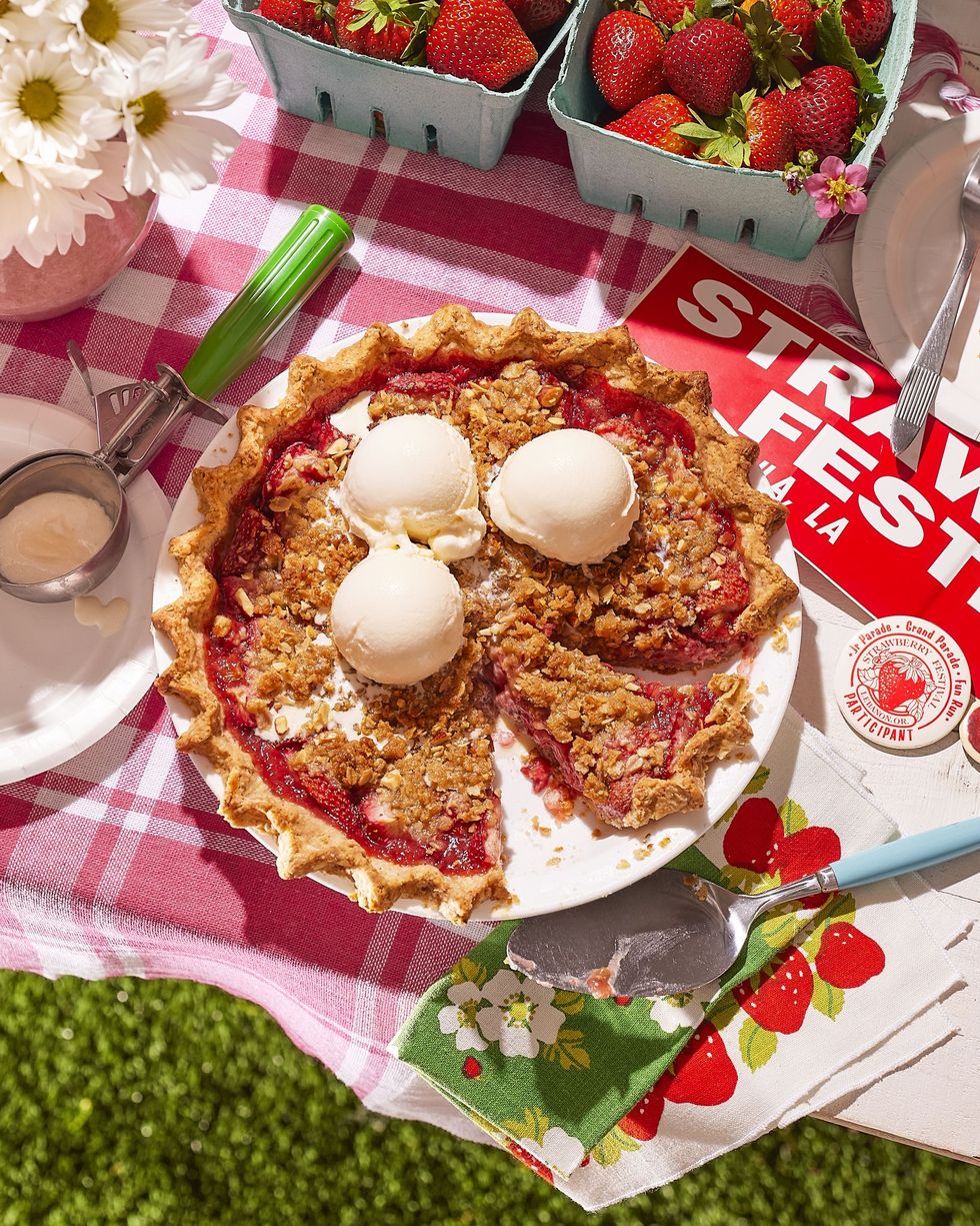 strawberry almond crumble pie in a white pie dish on a picnic table and topped with three scoops of vanilla ice cream