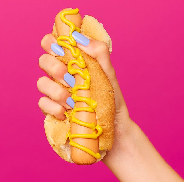 hand with lilac nail polish squishing hot dog with mustard