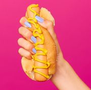 hand with lilac nail polish squishing hot dog with mustard