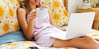 woman laying in bed with laptop and coffee mug in pajamas