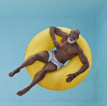 summer quotes bald senior man drinking juice while relaxing in yellow inflatable ring