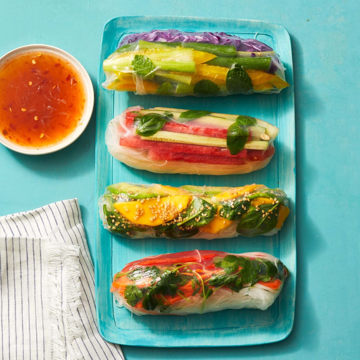 four summer rolls with veggie matchsticks wrapped in rice paper on a blue plate