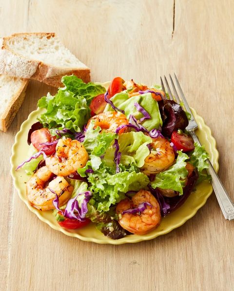 ginger shrimp salad with leafy greens on yellow plate with bread slices on side