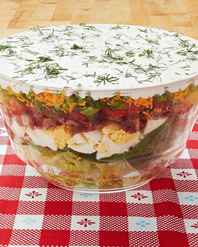 layered salad with dressing on top on red and white checkered cloth
