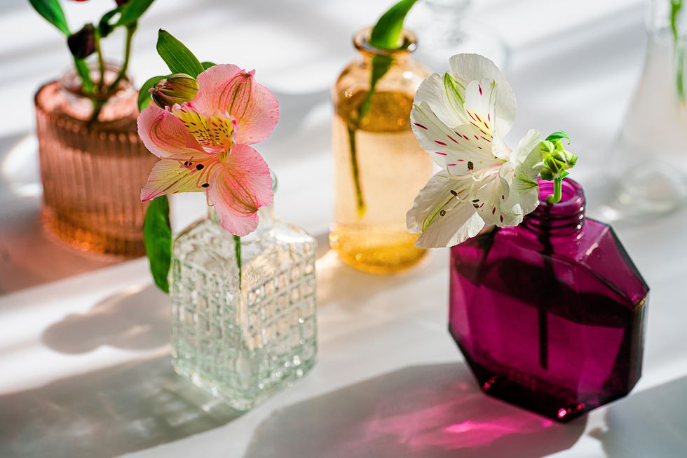 summer scene with flowers in the colorful glass vases from perfume sun and shadows minimal nature background