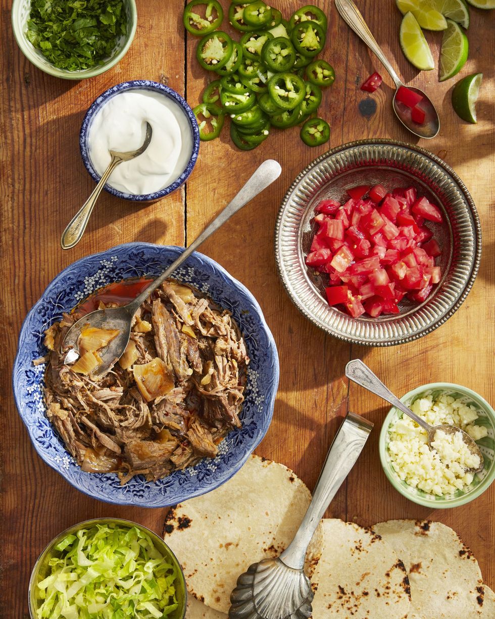 slow cooker beef tacos and toppings in bowls spread out on a wooden serving board