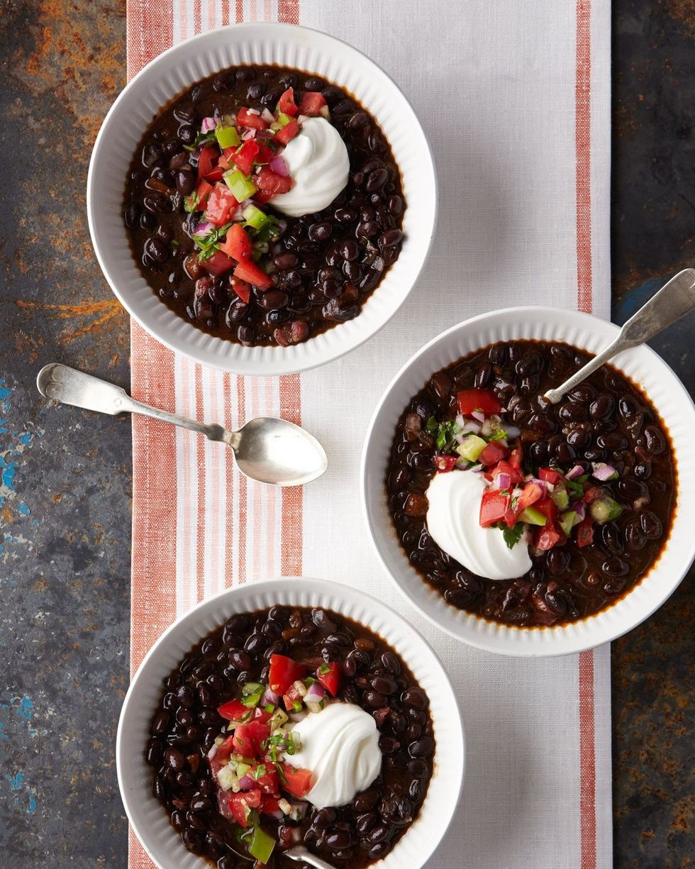 three bowls of slow cooker black bean and chile soup with sour cream and pico de gallo on top