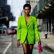 new york, new york   february 12 a guest wears gold large earrings, a gold large chain necklace, a green flashy blazer jacket, matching green flashy suit shorts, pearls bracelets, rings, a neon pink shiny leather micro handbag from balenciaga, outside song jun wan, during new york fashion week, on february 12, 2022 in new york city photo by edward berthelotgetty images