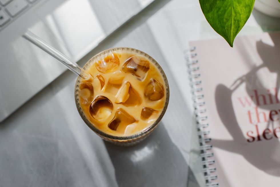 summer workspace composition. glass with ice latte, laptop and pot with houseplant on white office table. morning shadow. flat lay, view from above.