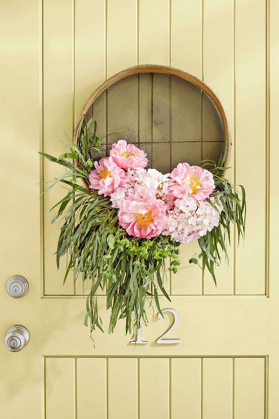 vintage grain sifter turned into a summer door wreath with pink flowers and greenery filling the lower curve