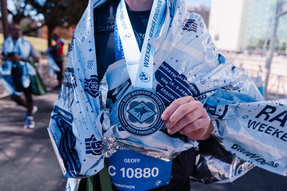 runner holding a finishers medal wearing a reflective blanket at dallas marathon 2023