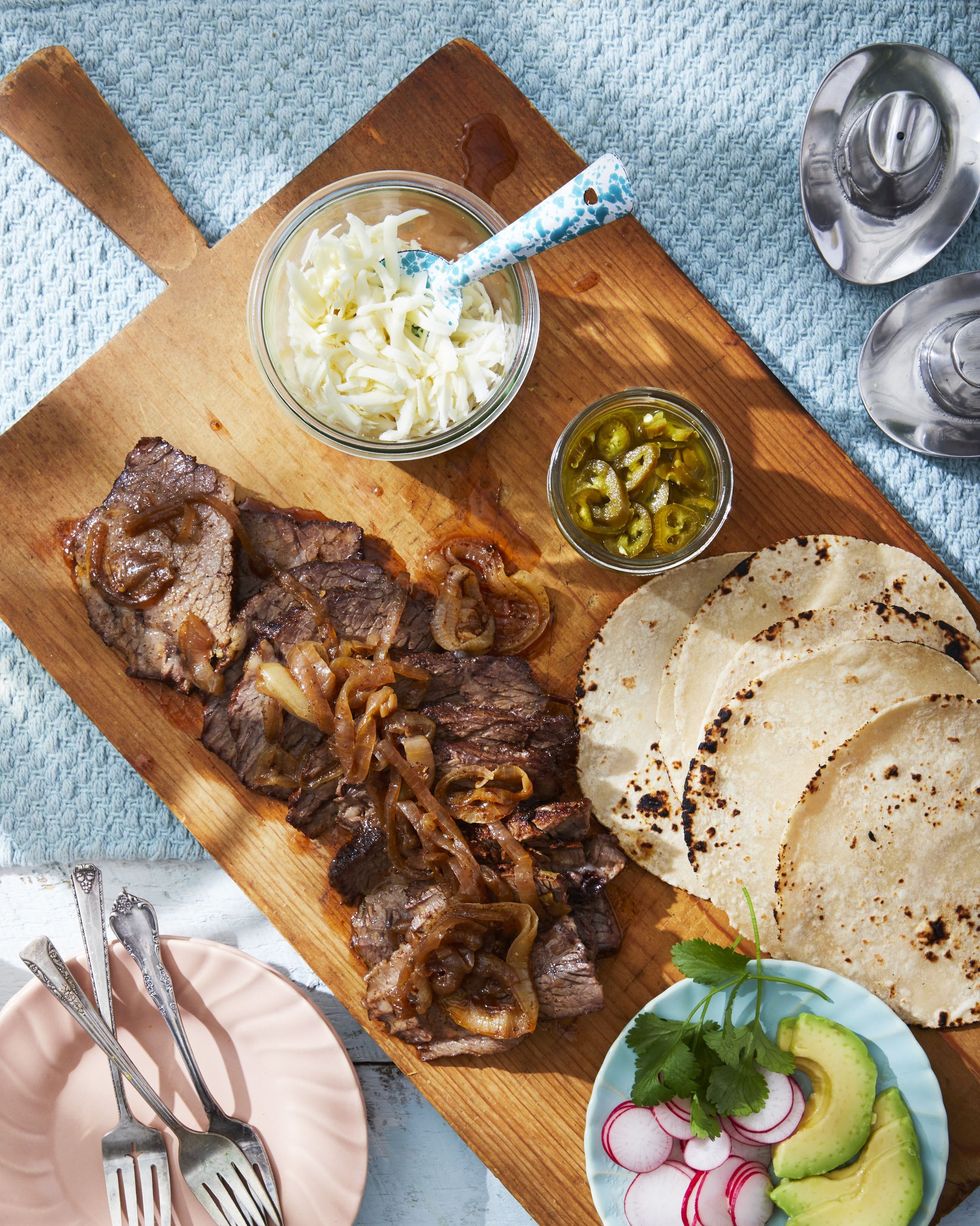 oven brisket on a wooden serving board with grilled tortillas and small bowls of toppings for tacos