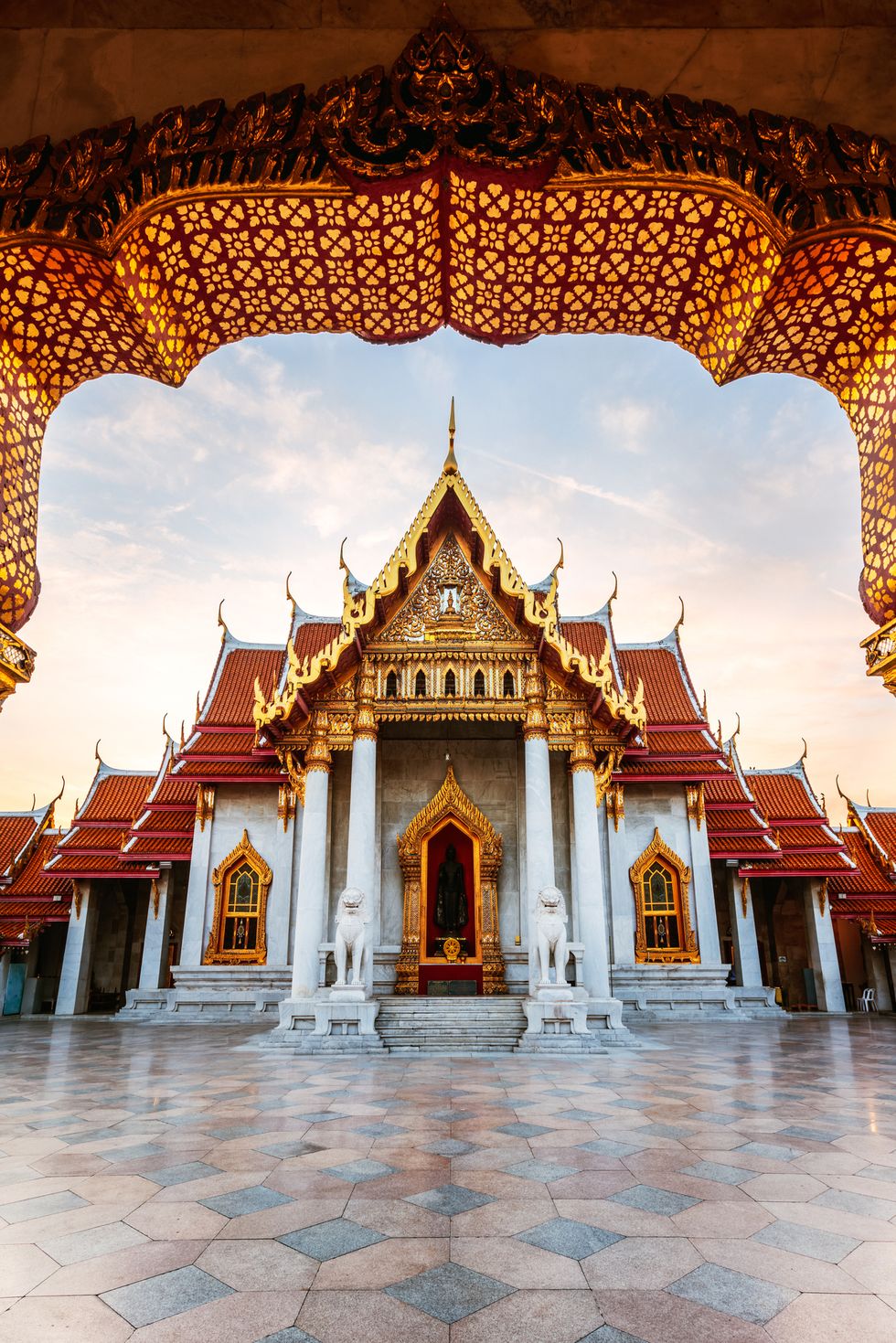 sunrise at marble temple, thailand with an exterior of gold arches and dorrways, white marble columns and geometrically tiled marble courtyard