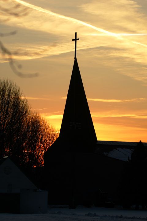 a cross atop a steeple receives a heavenly seal of approval with a cross etched on a cloudscape by the setting sun