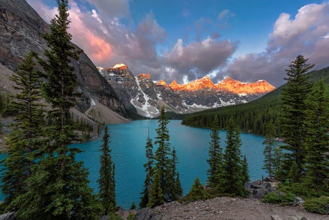 Prachtige zonsopgang boven het turkooizen water van het Moraine Lake met erboven de besneeuwde en rood oplichtende toppen van de Canadese Rockies in het Banff National Park Ik reis de hele wereld rond en kon me niet herinneren dat iets z tot de verbeelding sprak Het Moraine Lake is echt een ongelooflijk tafereel Het eerste halfuur kon ik het zelfs niet fotograferen  ik zat gewoon te genieten van deze schoonheid Ik wil weer naar deze plek terugkeren en ik weet zeker dat het nooit zal vervelen Het is echt iets wat je met eigen ogen moet zien