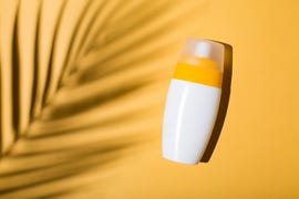 sunscreen on a yellow background with shadow of tropical leaf