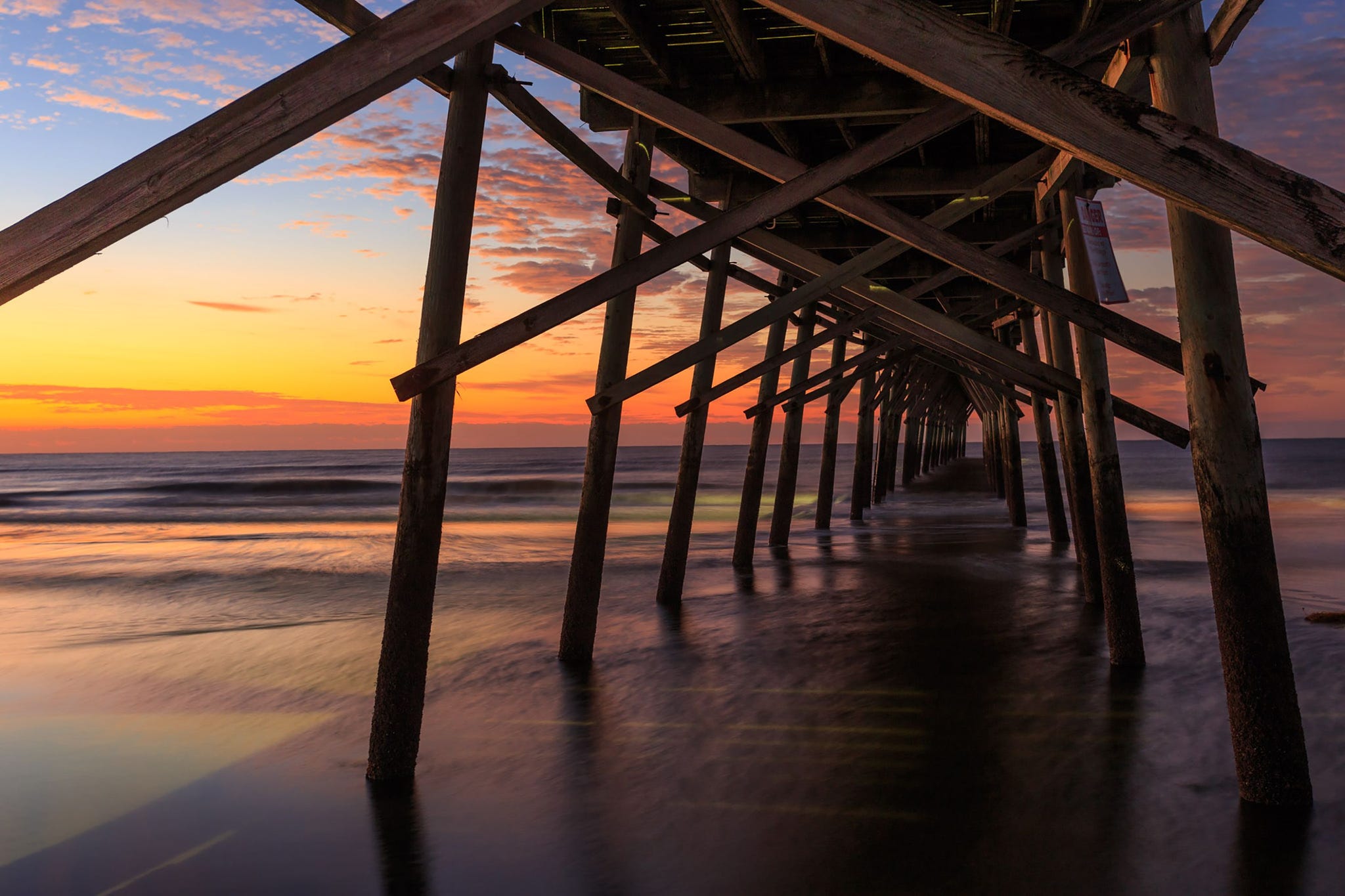 Onder de pier van Sunset Beach op Brunswick Island North Carolina kleurt de zonsondergang de lucht in prachtige schakeringen