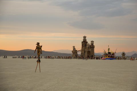 Een deelnemer aan het Burning Manfestival loopt op stelten door de woestijn terwijl hij grote kunstinstallaties achter zich laat