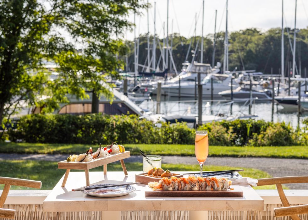 sushi and a cocktail sit on a platter overlooking a marina at sunset harbor restaurant in the hamptons