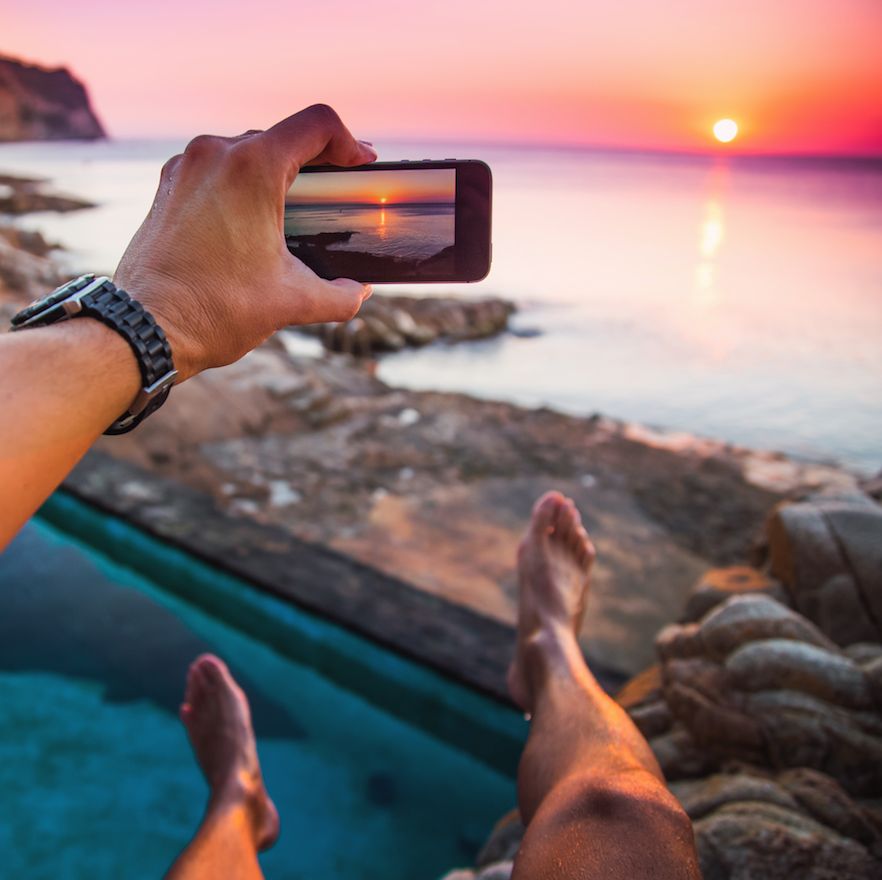 Guy from personal perspective taking pictures with smartphone from a natural pool in the Mediterranean Sea Costa Brava shoreline watching the sunrise with his legs levitating in the air during summer time.