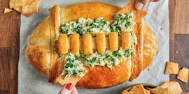 spinach and artichoke dip in a bread bowl shaped like a football