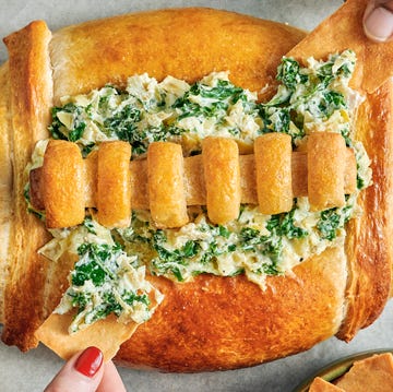 spinach and artichoke dip in a bread bowl shaped like a football