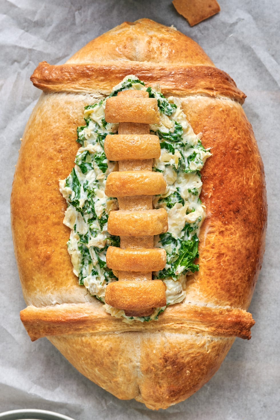 spinach and artichoke dip in a bread bowl shaped like a football