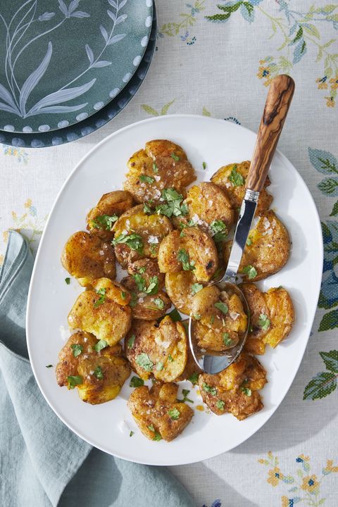 smashed potatoes with paprika and cumin on an oval white plate with a spoon for serving